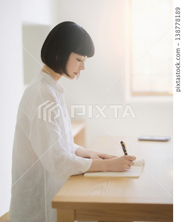 一位女士側臉凝視著自己，神情專注地在書桌前的筆記本上書寫。 138778189