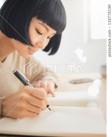 一位女士用鋼筆在筆記本上寫字，她的手和側臉清晰可見。 138778190