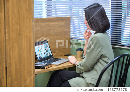 一位女商人坐在靠窗的隔間座位上，側身觀看線上會議。 138778278