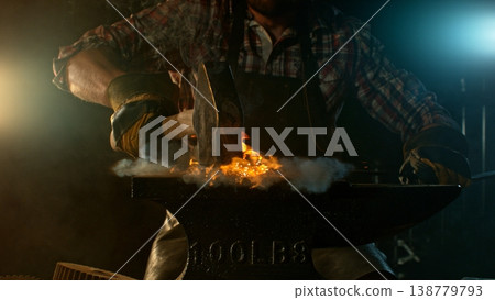 Close-up of blacksmith forging glowing hot iron on anvil with flying sparks 138779793