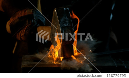 Close-up of blacksmith forging glowing hot iron on anvil with flying sparks Close-up of blacksmith forging glowing hot iron on anvil with flying sparks 138779795
