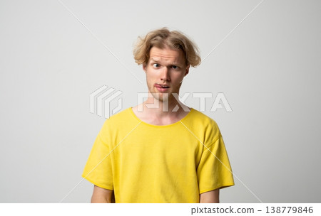 Young blonde man making a silly face, crossing one eye and sticking out his tongue, expressing a playful and foolish mood on a neutral background 138779846