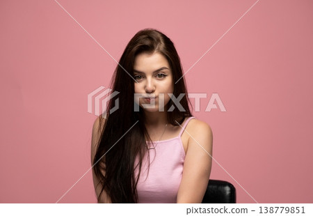 Young woman making a funny face, puffing cheeks, having fun in a studio portrait against a pink background Young woman making a funny face, puffing cheeks, having fun in a studio portrait against a pink background 138779851