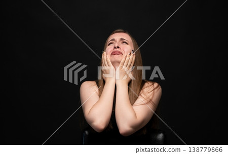 Young woman covering her face while crying, experiencing sadness, grief, and emotional pain against a dark background 138779866