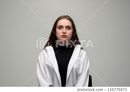 Young woman posing in a studio for a headshot, wearing a white shirt over a black top with long brown hair Young woman posing in a studio for a headshot, wearing a white shirt over a black top with long brown hair 138779873