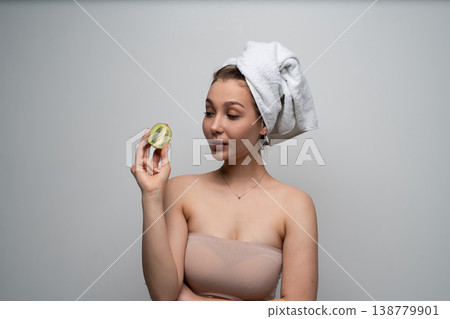 Woman holding half kiwi looking at fruit, having a spa treatment for skin care and natural beauty, promoting wellness and a healthy lifestyle Woman holding half kiwi looking at fruit, having a spa treatment for skin care and natural beauty, promoting wellness and a healthy lifestyle 138779901