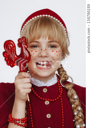 Smiling Caucasian girl with rooster lollipop in Russian folk style outfit on light background 138780289