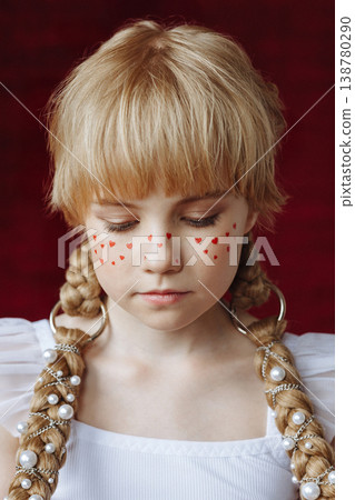 Thoughtful Caucasian girl with braids and heart makeup looking down on red background Thoughtful Caucasian girl with braids and heart makeup looking down on red background 138780290