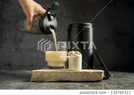Pouring protein vanilla shake in drinking glass and scoop with whey protein powder on dark background Pouring protein vanilla shake in drinking glass and scoop with whey protein powder on dark background 138780321