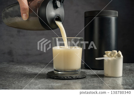 Pouring protein vanilla shake in drinking glass and scoop with whey protein powder on dark background Pouring protein vanilla shake in drinking glass and scoop with whey protein powder on dark background 138780340