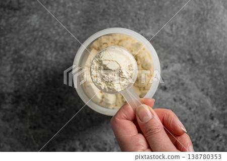 Female hands holding a scoop of protein whey powder, white plastic tube, on dark background Female hands holding a scoop of protein whey powder, white plastic tube, on dark background 138780353