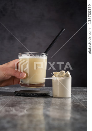 Protein vanilla shake and scoop with whey protein powder on dark background, female hand Protein vanilla shake and scoop with whey protein powder on dark background, female hand 138780359