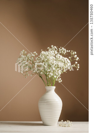 White floral background. Soft home decor, vase with white small flowers on white background, copy space White floral background. Soft home decor, vase with white small flowers on white background, copy space 138780460