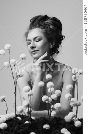 Young Caucasian redhead woman touching face among dried white flowers on moss, white wall Young Caucasian redhead woman touching face among dried white flowers on moss, white wall 138780464