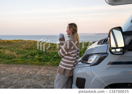 Woman drinking coffee by campervan enjoying peaceful coastal landscape during travel journey Woman drinking coffee by campervan enjoying peaceful coastal landscape during travel journey 138780635
