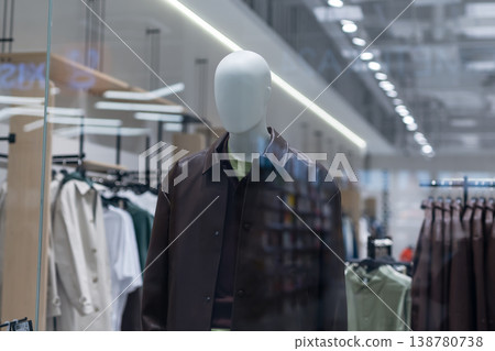 Refined mannequin posed in brightly lit display with glass surfaces and retail fixtures 138780738