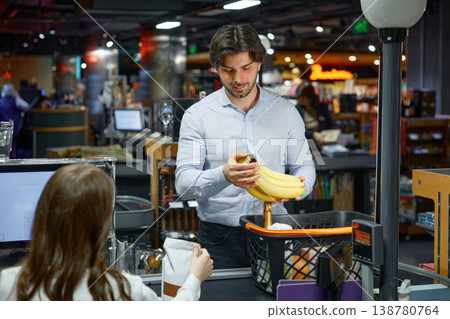 A man is putting ripe bananas from basket on the checking belt inside a grocery store 138780764