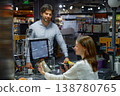 A man customer standing at a cash register inside a store, while woman is scanning the products 138780765