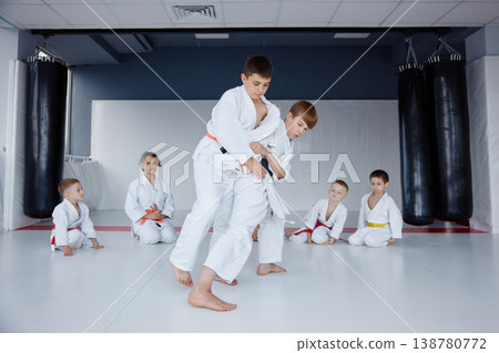 Young judo students practice throws in modern dojo with coach supervising Young judo students practice throws in modern dojo with coach supervising 138780772