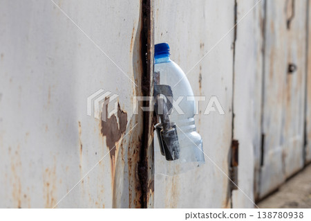 A garage door is closed and a plastic water bottle is used to secure the locking mechanism. The scene shows a typical afternoon A garage door is closed and a plastic water bottle is used to secure the locking mechanism. The scene shows a typical afternoon 138780938