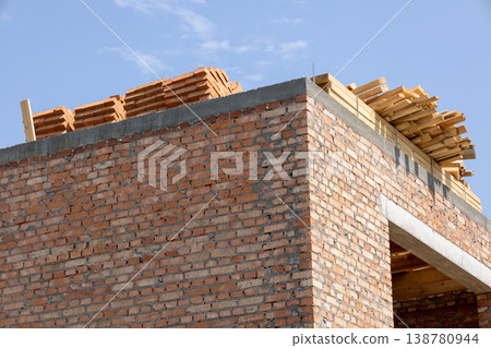 Construction workers are building a house with stacked materials on the roof and brick walls being built under clear blue sky Construction workers are building a house with stacked materials on the roof and brick walls being built under clear blue sky 138780944