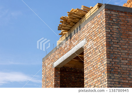 New house construction shows brick walls with wooden beams stacked on top under a clear sky New house construction shows brick walls with wooden beams stacked on top under a clear sky 138780945
