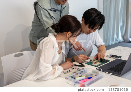 A young man and woman are studying electronic circuits with the help of an engineer. A young man and woman are studying electronic circuits with the help of an engineer. 138781016