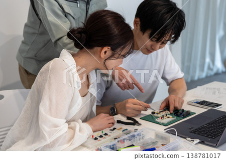 A young man and woman are studying electronic circuits with the help of an engineer. A young man and woman are studying electronic circuits with the help of an engineer. 138781017