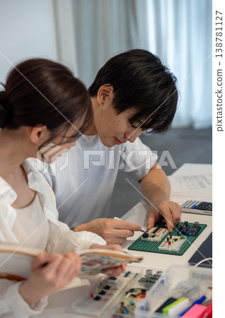 A young man and woman studying electronic circuits while looking at a textbook. 138781127
