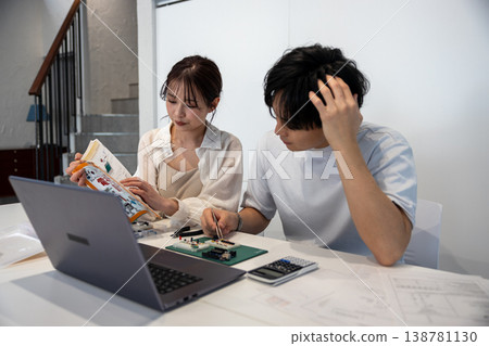 一對年輕男女正在看著教科書研究電子電路。 一對年輕男女正在看著教科書研究電子電路。 138781130
