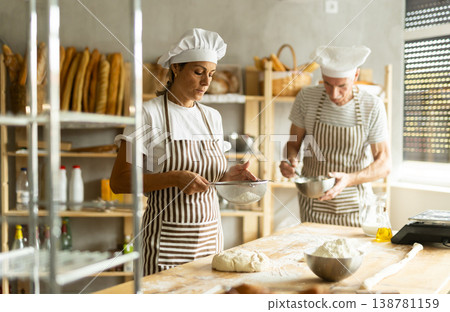 Elderly man and woman sift flour and whipping dough Elderly man and woman sift flour and whipping dough 138781159