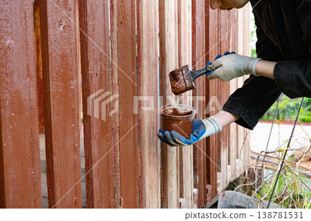 Painting wooden fence with brown paint during daytime Painting wooden fence with brown paint during daytime 138781531
