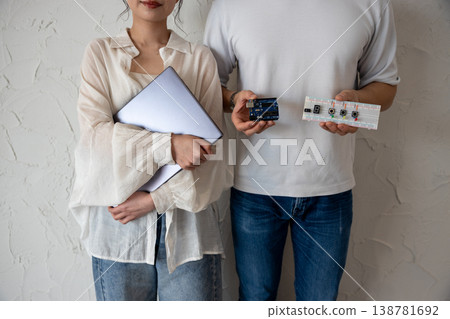 一對年輕男女站在牆前,手裡拿著電子電路和一台電腦。 一對年輕男女站在牆前,手裡拿著電子電路和一台電腦。 138781692