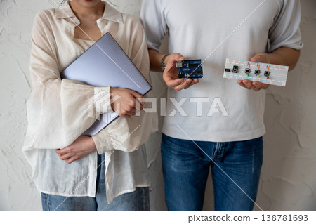 一對年輕男女站在牆前,手裡拿著電子電路和一台電腦。 一對年輕男女站在牆前,手裡拿著電子電路和一台電腦。 138781693
