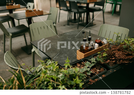 Close-up of a cafe table framed by greenery, with bottles of oil and vinegar catching soft light like a quiet promise of flavor 138781782