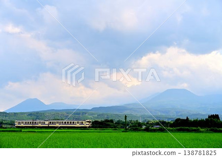 A local train running with the Kirishima mountain range in the background. A local train running with the Kirishima mountain range in the background. 138781825
