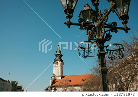 Historic church tower with decorative street lamp in foreground under blue sky in Sombor, Serbia, urban European architecture 138781978
