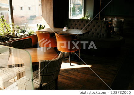 Modern cafe interior with wooden tables, soft chairs and warm sunlight through window. Concept of comfort, hospitality and stylish dining space 138782000