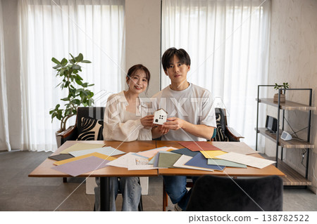 A young couple is facing the camera, holding crafts of houses of different sizes. 138782522