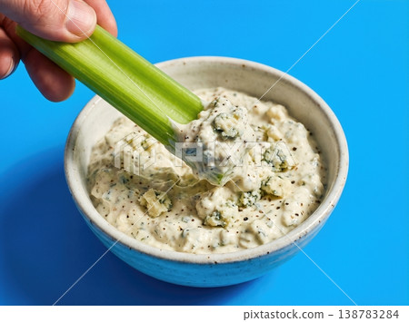 Hand Dipping a Crisp Celery Stick into Blue Cheese Dressing Isolated on a Solid Bright Blue Background Hand Dipping a Crisp Celery Stick into Blue Cheese Dressing Isolated on a Solid Bright Blue Background 138783284