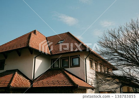 Residential building with traditional red clay tile roof and bare tree branches under blue sky in Balkans, Bosnia. Concept of suburban architecture, housing and peaceful neighborhood life Residential building with traditional red clay tile roof and bare tree branches under blue sky in Balkans, Bosnia. Concept of suburban architecture, housing and peaceful neighborhood life 138783855