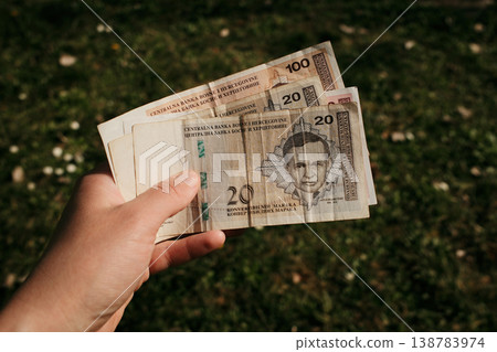 Hand holding Bosnia and Herzegovina convertible mark banknotes of different values against blurred grass background. Concept of cash payment, Balkan economy and financial management 138783974