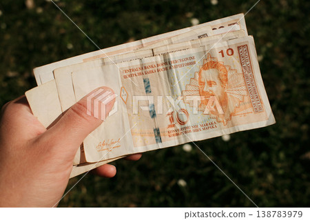 Hand holding Bosnia and Herzegovina 10 convertible mark banknote outdoors in natural sunlight. Concept of Balkan currency, cash payment and everyday financial exchange 138783979