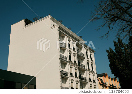 Elegant white residential building with classical architecture and balconies under a clear blue sky. Modern urban real estate combining traditional style with contemporary living Elegant white residential building with classical architecture and balconies under a clear blue sky. Modern urban real estate combining traditional style with contemporary living 138784003