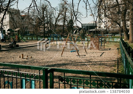 Empty children recreation ground with swings and climbing structures surrounded by residential buildings. Outdoor leisure area designed for activity, movement, and childhood development 138784030