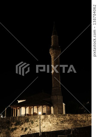 Night view of a mosque with illuminated minaret beside stone residential buildings in Mostar under a dark sky Night view of a mosque with illuminated minaret beside stone residential buildings in Mostar under a dark sky 138784062