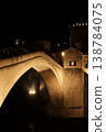 The iconic stone bridge of Mostar glows under night lighting above the river. Historic architecture and dramatic contrast highlight the landmark against the dark sky 138784075