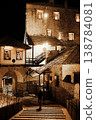 Night view of historic stone buildings in Mostar old town, illuminated with warm lights, showing traditional architecture, wooden roofs, stairway and a single person standing on old bridge. 138784081