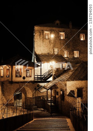Night view of historic stone buildings in Mostar illuminated by warm lights. Traditional Balkan architecture and quiet atmosphere emphasize the timeless character of the old town Night view of historic stone buildings in Mostar illuminated by warm lights. Traditional Balkan architecture and quiet atmosphere emphasize the timeless character of the old town 138784093