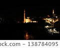 Night view of the historic old town in Mostar with illuminated stone houses, mosque minarets, riverside cafes and warm lights reflecting along the Neretva River 138784095